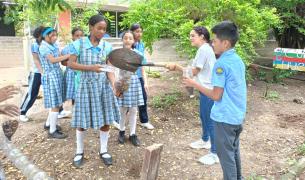 Students in school uniform stand outside holding shovels and bottles as they participate in a science experiment