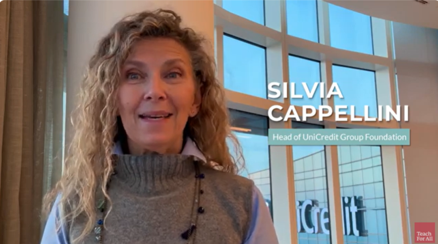 Headshot of a white woman with long curly blond hair in a grey sweater next to onsrcreen text of her name and title, Silvia Capellini, Head of Unicredit Group Foundation