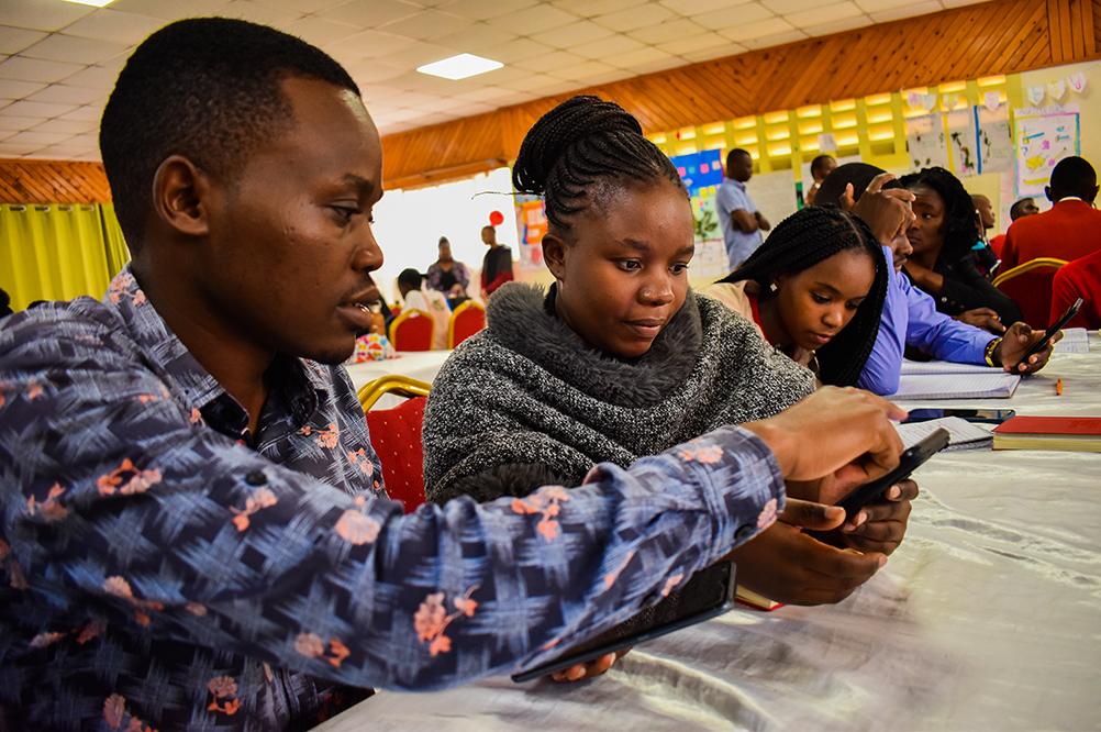 A young Black man points to something on a digital device in a young black woman's hand