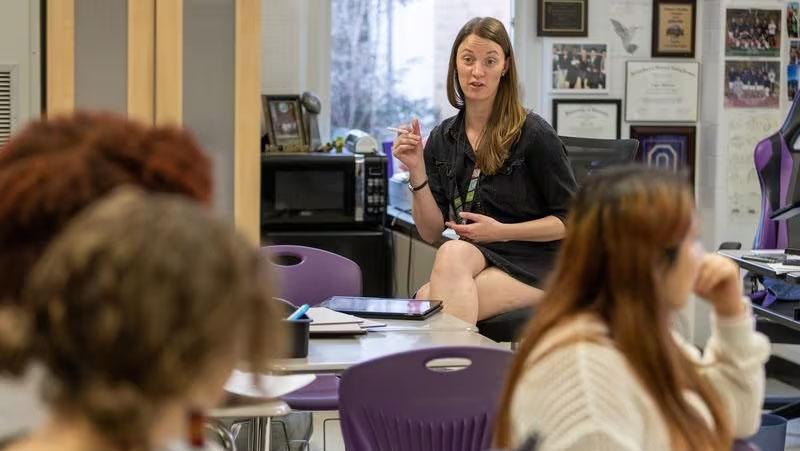 A young woman address a class of high school students