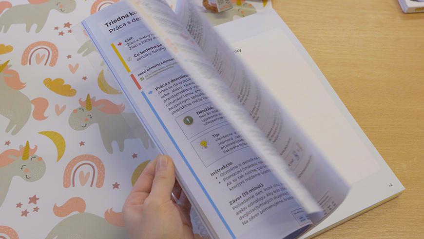 A hand flipping through a workbook laid on a desk